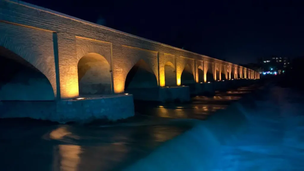 پل تاریخی مارنان اصفهان هنگام غروب با نورپردازی طاقهای پل در کنار زایندهرود